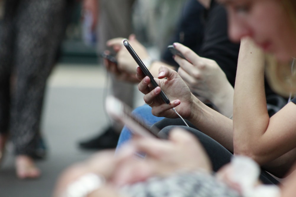 Multiple people sitting in a row and looking at their smartphones